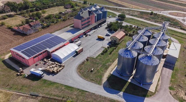 Aerial view of storage silo Bavaniste featuring large metallic grain silos a facility building with solar panels and a paved yard with trucks in Bavaniste Vojvodina Serbia.