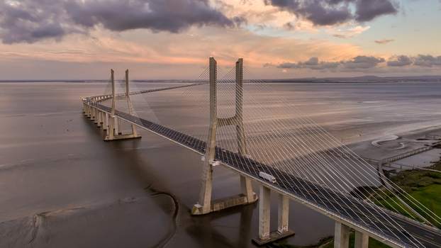 Aerial view of the Vasco da Gama Bridge spanning the Tagus River under a dramatic sunset sky with soft clouds Lisboa Portugal.