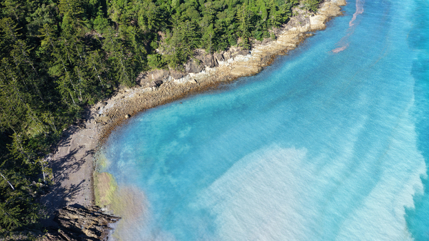 Aerial view of Chance Bay featuring turquoise waters a sandy beach and lush green forest along the coastline in Whitsundays Queensland Australia. Aerial view of Chance Bay featuring turquoise waters a sandy beach and lush green forest along the coastline in Whitsundays Queensland Australia.