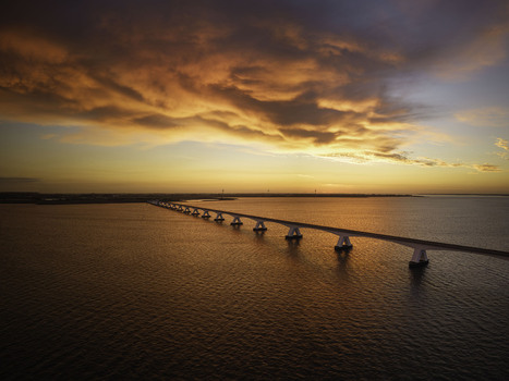 Aerial view of the Zeeland Bridge spanning the Oosterschelde estuary during a vibrant sunrise with orange clouds reflecting on the water in Zierikzee Zeeland Netherlands. Aerial view of the Zeeland Bridge spanning the Oosterschelde estuary during a vibrant sunrise with orange clouds reflecting on the water in Zierikzee Zeeland Netherlands.