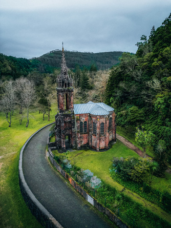Aerial view of the abandoned gothic church stands in stark contrast against the vibrant green landscape with a winding path leading to its weathered stone walls Furnas Portugal.