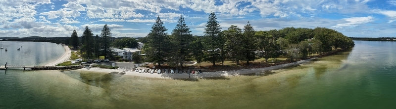 Aerial view of a tranquil peninsula with tall pines casting shadows on the sandy beach contrasting with the clear turquoise waters Forster New South Wales Australia.