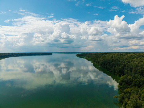 Aerial view of Kaunas Reservoir with lush green forests along the shoreline and fluffy white clouds reflected in the calm water in Kaunas Kaunas County Lithuania.