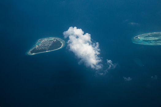 Aerial view of islands surrounded by turquoise waters with white clouds casting shadows over the serene seascape Flight from Male to Hanimaadhoo island Maldives.