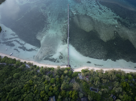 Aerial view of a long wooden pier extending into clear turquoise sea waters near Labuan Bajo surrounded by lush tropical greenery and sandy beach in Komodo East Nusa Tenggara Indonesia. Aerial view of a long wooden pier extending into clear turquoise sea waters near Labuan Bajo surrounded by lush tropical greenery and sandy beach in Komodo East Nusa Tenggara Indonesia.