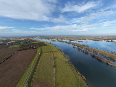 Aerial view of a winding river flowing through green agricultural fields and meadows under a bright blue sky in the Netherlands. Aerial view of a winding river flowing through green agricultural fields and meadows under a bright blue sky in the Netherlands.