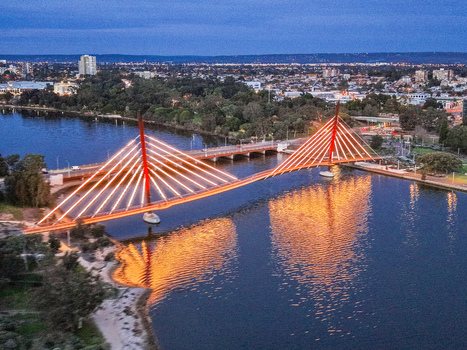Aerial view of the illuminated Boorloo Bridge spanning the Swan River at dusk with city skyline and parkland in the background in East Perth Western Australia Australia.