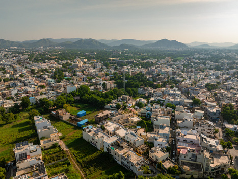 Aerial view of the cityscape of Udaipur showing residential buildings lush green trees and distant hills under a clear sky in Udaipur Rajasthan India.