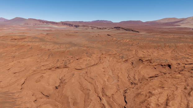 Aerial view of the vast arid reddish brown desert landscape with a winding dirt road cutting through rugged terrain in Tolar Grande Salta Province Argentina. Aerial view of the vast arid reddish brown desert landscape with a winding dirt road cutting through rugged terrain in Tolar Grande Salta Province Argentina.