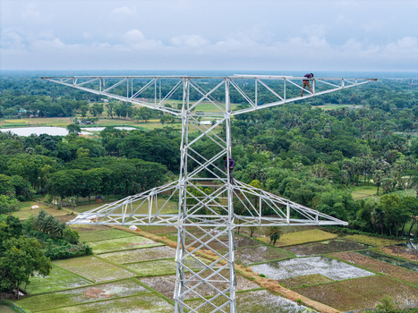 Trishal Upazila Bangladesh 13 May 2026 Aerial view of workers climbing a high voltage electricity pylon overlooking lush green agricultural fields and rural landscape. Trishal Upazila Bangladesh 13 May 2026 Aerial view of workers climbing a high voltage electricity pylon overlooking lush green agricultural fields and rural landscape.