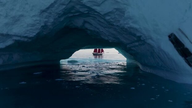 Aerial view of red sailed ship through ice arch in Greenland. Aerial view of red sailed ship through ice arch in Greenland.