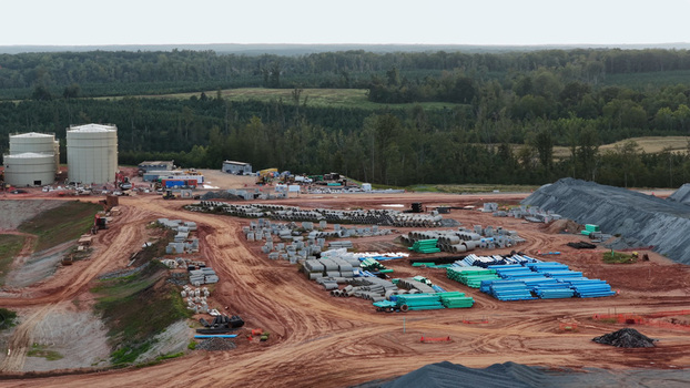 Aerial view of a construction site featuring large storage tanks stacks of concrete and blue pipes and dirt access roads surrounded by a forest in Louisa County Virginia United States. Aerial view of a construction site featuring large storage tanks stacks of concrete and blue pipes and dirt access roads surrounded by a forest in Louisa County Virginia United States.