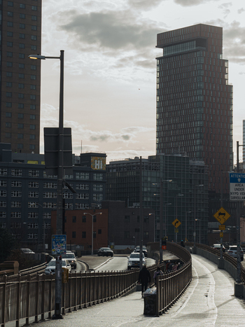 View of the Brooklyn Bridge pedestrian walkway with modern skyscrapers in the background street signs and people walking in Kings County New York United States.