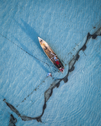 Aerial view of a boat resting in the turquoise water its long shadow stretching across the rippled surface Lembongan Bali Indonesia. Aerial view of a boat resting in the turquoise water its long shadow stretching across the rippled surface Lembongan Bali Indonesia.