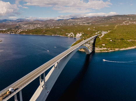Aerial view of the Krk Bridge spanning the Adriatic Sea with boats navigating the blue waters near the coastal landscape of Smrika Primorje Gorski Kotar Croatia. Aerial view of the Krk Bridge spanning the Adriatic Sea with boats navigating the blue waters near the coastal landscape of Smrika Primorje Gorski Kotar Croatia.