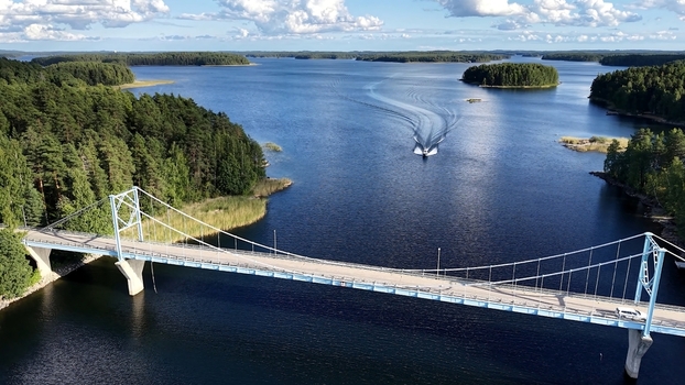 Aerial view of the Potkusalmen silta Bridge spanning a serene lake with a boat cruising through the water surrounded by lush pine forests in Savonlinna Etela Savo Finland. Aerial view of the Potkusalmen silta Bridge spanning a serene lake with a boat cruising through the water surrounded by lush pine forests in Savonlinna Etela Savo Finland.