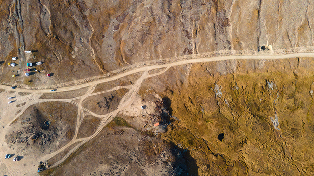 Aerial view of Deosai National Park featuring a winding dirt road scattered tents and rugged high altitude terrain in Skardu Gilgit Pakistan.