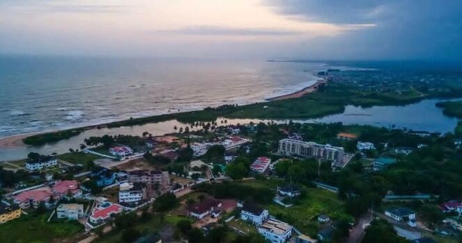 Aerial view of the coastline in Ghana featuring a river inlet meeting the ocean surrounded by residential buildings lush greenery and sandy shores. Ghana. Aerial view of the coastline in Ghana featuring a river inlet meeting the ocean surrounded by residential buildings lush greenery and sandy shores. Ghana.