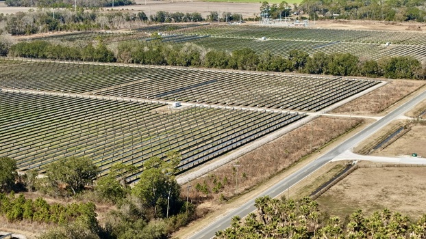 Aerial view of a vast solar farm shimmering under the sunlight contrasting with the surrounding dry fields and distant power lines Elkton Florida United States. Aerial view of a vast solar farm shimmering under the sunlight contrasting with the surrounding dry fields and distant power lines Elkton Florida United States.