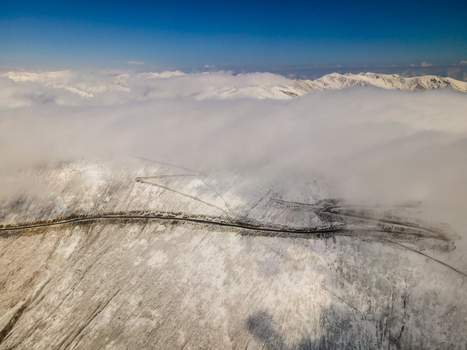 Aerial view of the winding mountain road of Babusar Pass covered in fresh snow under a thick layer of clouds and a clear blue sky in Babusar KPK Pakistan. Aerial view of the winding mountain road of Babusar Pass covered in fresh snow under a thick layer of clouds and a clear blue sky in Babusar KPK Pakistan.
