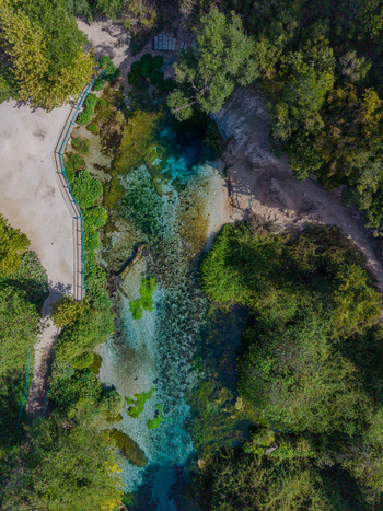 Aerial view of The Blue Eye a natural spring with vibrant turquoise water surrounded by lush green forest and walking paths in Saranda Qarku i Vlores Albania. Aerial view of The Blue Eye a natural spring with vibrant turquoise water surrounded by lush green forest and walking paths in Saranda Qarku i Vlores Albania.