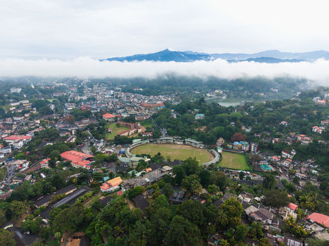 Aerial view of Bogambara Stadium and the urban landscape of Kandy surrounded by lush green hills and misty mountains under a layer of clouds Kandy Central Province Sri Lanka. Aerial view of Bogambara Stadium and the urban landscape of Kandy surrounded by lush green hills and misty mountains under a layer of clouds Kandy Central Province Sri Lanka.
