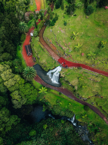 Aerial view of vibrant red paths wind past a cascading waterfall embraced by verdant forest creating a striking contrast of color and texture Achada Açores Portugal. Aerial view of vibrant red paths wind past a cascading waterfall embraced by verdant forest creating a striking contrast of color and texture Achada Açores Portugal.