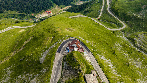 Aerial view of the Transfagarasan mountain pass winding through green mountains with a lodge on a sharp curve in Curtea de Arges Judetul Arges Romania. Aerial view of the Transfagarasan mountain pass winding through green mountains with a lodge on a sharp curve in Curtea de Arges Judetul Arges Romania.