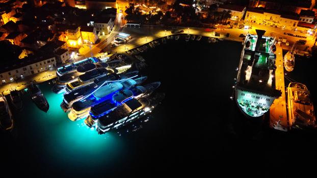 Aerial view of the harbor with boats and the illuminated waterfront buildings casting vibrant reflections on the dark waters Bol Croatia.