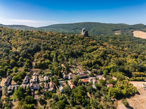 Aerial view of Holloko Castle rising above the traditional old village surrounded by forested hills rural homes and fields in Holloko Hungary during late summer. Aerial view of Holloko Castle rising above the traditional old village surrounded by forested hills rural homes and fields in Holloko Hungary during late summer.