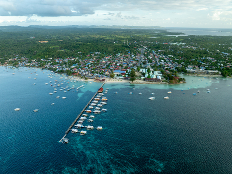 Aerial view of the coastal town of General Luna with a long wooden pier numerous outrigger boats turquoise waters and lush tropical vegetation in General Luna Siargao Philippines. Aerial view of the coastal town of General Luna with a long wooden pier numerous outrigger boats turquoise waters and lush tropical vegetation in General Luna Siargao Philippines.