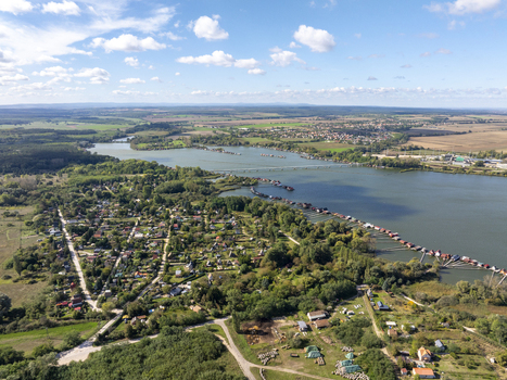 Aerial view of Bokodi Floating Village with its iconic wooden houses on stilts over the lake surrounded by lush greenery and rural landscape in Oroszlany Hungary. Aerial view of Bokodi Floating Village with its iconic wooden houses on stilts over the lake surrounded by lush greenery and rural landscape in Oroszlany Hungary.