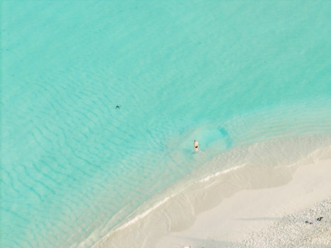 Aerial view of the serene meeting of white sand and turquoise waters where a lone figure wades gently Dhidhdhoo Thiladhunmathi Atoll Maldives.