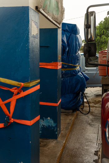San Jose Tinian Northern Mariana Islands 05 July 2026 View of a blue pillar secured with orange straps and blue tarp covered cargo near a truck in a local business area. San Jose Tinian Northern Mariana Islands 05 July 2026 View of a blue pillar secured with orange straps and blue tarp covered cargo near a truck in a local business area.