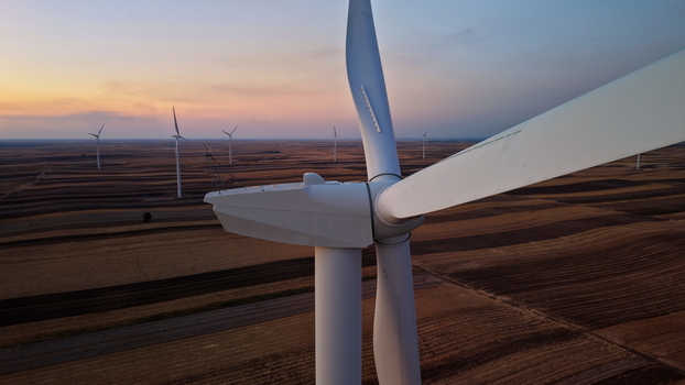 Aerial view of a large wind turbine standing in a vast agricultural field during the golden hour with a soft sunset sky in Vladimirovac Vojvodina Serbia. Aerial view of a large wind turbine standing in a vast agricultural field during the golden hour with a soft sunset sky in Vladimirovac Vojvodina Serbia.