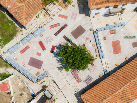 Aerial view of traditional carpets and rugs displayed in a stone courtyard with a central tree and terracotta rooftops in Dhermi Vlore County Albania. Aerial view of traditional carpets and rugs displayed in a stone courtyard with a central tree and terracotta rooftops in Dhermi Vlore County Albania.