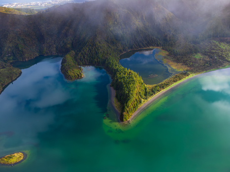 Aerial view of Lagoa do Fogo crater lake featuring turquoise water and a forested peninsula under misty volcanic hills in Agua de Alto Azores Portugal. Aerial view of Lagoa do Fogo crater lake featuring turquoise water and a forested peninsula under misty volcanic hills in Agua de Alto Azores Portugal.