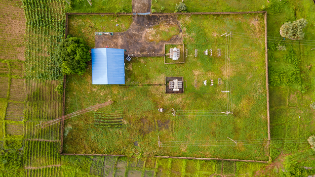 Aerial view of a small electrical substation with transformers and power lines inside a fenced enclosure surrounded by lush green farmland in Minna Niger State Nigeria. Aerial view of a small electrical substation with transformers and power lines inside a fenced enclosure surrounded by lush green farmland in Minna Niger State Nigeria.