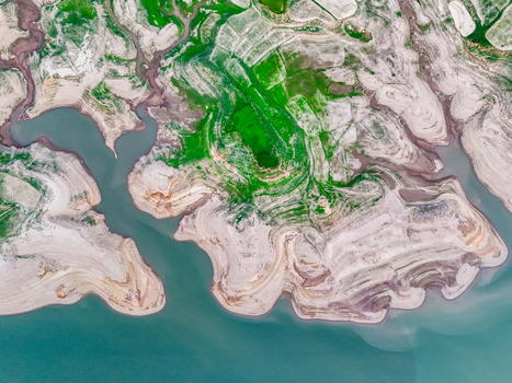 Aerial view of the intricate patterns of water meeting land with vibrant green vegetation interspersed with pale earth tones Chakswari Azad Kashmir Pakistan. Aerial view of the intricate patterns of water meeting land with vibrant green vegetation interspersed with pale earth tones Chakswari Azad Kashmir Pakistan.