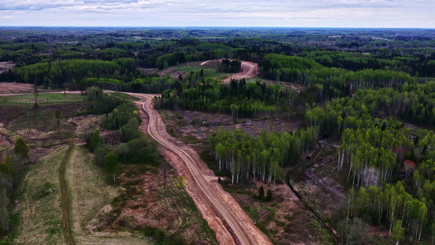 Aerial view of a dirt wind turbine maintenance access road winding through a dense forest landscape in Latvia. Aerial view of a dirt wind turbine maintenance access road winding through a dense forest landscape in Latvia.