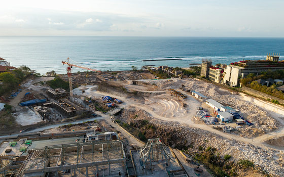 Aerial view of a resort development construction site with a tall crane heavy machinery and partially built structures overlooking the ocean in Kecamatan Kuta Selatan Bali Indonesia. Aerial view of a resort development construction site with a tall crane heavy machinery and partially built structures overlooking the ocean in Kecamatan Kuta Selatan Bali Indonesia.