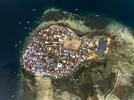 Aerial view of Pulau Mesa island village with dense housing a central open area and small boats moored in the surrounding turquoise waters of Kecamatan Komodo Nusa Tenggara Timur Indonesia. Aerial view of Pulau Mesa island village with dense housing a central open area and small boats moored in the surrounding turquoise waters of Kecamatan Komodo Nusa Tenggara Timur Indonesia.