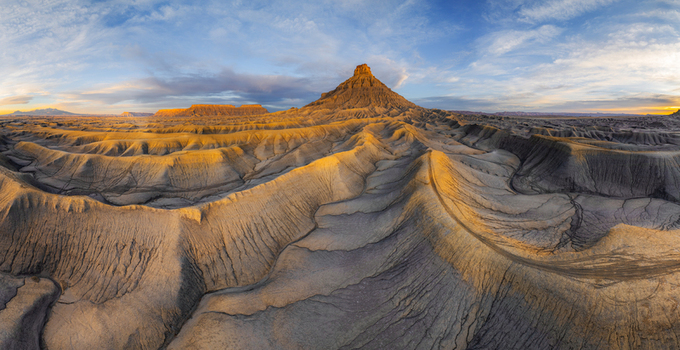 Aerial view of the badlands near Hanksville featuring eroded desert terrain and a prominent peak illuminated by golden hour light under a vast sky Hanksville Utah United States.