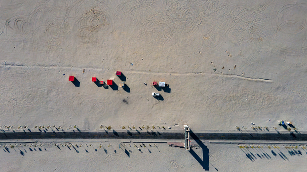 Aerial view of Sarfaranga Cold Desert in Shigar with scattered red structures a white vehicle and tire tracks on the sand near a paved road in Skardu Gilgit Pakistan. Aerial view of Sarfaranga Cold Desert in Shigar with scattered red structures a white vehicle and tire tracks on the sand near a paved road in Skardu Gilgit Pakistan.