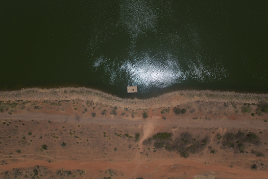 Aerial view of the Minjibir reservoir shoreline with dark green water sun reflection and arid reddish brown land in Kano Kano State Nigeria. Aerial view of the Minjibir reservoir shoreline with dark green water sun reflection and arid reddish brown land in Kano Kano State Nigeria.