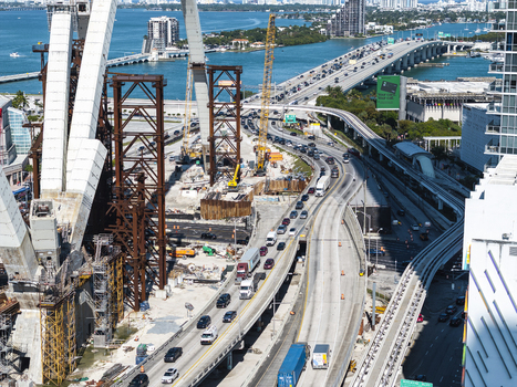 Aerial view of construction of the Signature Bridge with its dramatic arches heavy traffic on the MacArthur Causeway and the Miami skyline in the distance Miami Florida USA. Aerial view of construction of the Signature Bridge with its dramatic arches heavy traffic on the MacArthur Causeway and the Miami skyline in the distance Miami Florida USA.