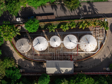 Aerial view of industrial storage tanks connected by a network of pipes surrounded by lush tropical trees and paved roads in Bajos de Haina San Cristobal Province Dominican Republic.
