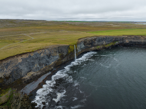 Aerial view of the cascading waterfall plunging from the rugged cliffs into the turbulent sea a stark contrast of nature s raw power H&uacute;nabygg&eth; Iceland.