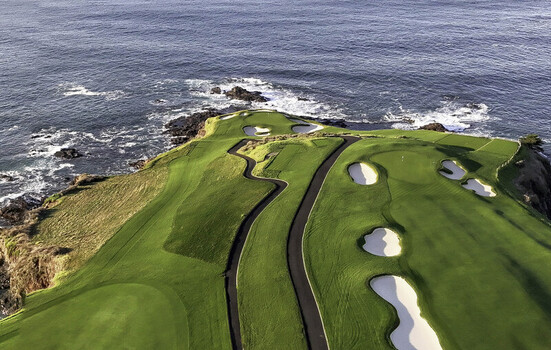 Aerial view of the 7th hole at Pebble Beach Golf Links featuring lush green fairways sand bunkers and rugged coastline along the Pacific Ocean in Pebble Beach CA United States. Aerial view of the 7th hole at Pebble Beach Golf Links featuring lush green fairways sand bunkers and rugged coastline along the Pacific Ocean in Pebble Beach CA United States.