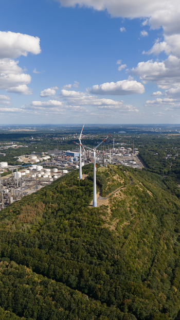 Aerial view of wind turbines on a forested hill overlooking the Tanklager industrial facility in Gelsenkirchen North Rhine Westphalia Germany.